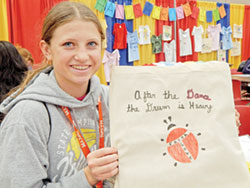 Freshman Natalie Bixenman of the Diocese of Salina, Kan., displays the tote bag she decorated for Hands Across Haiti, a ministry of St. John Paul II Parish in Sellersburg. (Photo by Mike Krokos)