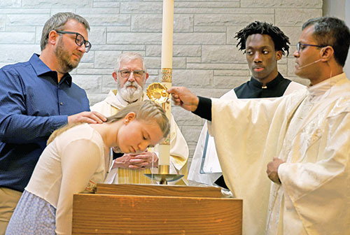 Father Sengole Thomas Gnanaraj baptizes 15-year-old Aubrey Bihl during the Easter Vigil Mass on March 31 at Holy Family Church in Richmond, one of three churches comprising St. Elizabeth Ann Seton Parish in east central Indiana. To her left is her sponsor and uncle, Mark Bihl, and behind the baptismal font is Deacon James Miller, who helped Aubrey on her path to Catholicism. Assisting Father Gnanaraj is altar server Kenny Gihozo. (Submitted photo by Dr. Sam Krutz)