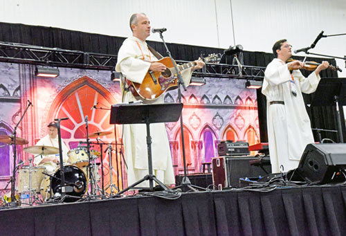 The Hillbilly Thomists play a concert on July 19 during the National Eucharistic Congress at the Indiana Convention Center in Indianapolis. They are, from left, drummer Dominican Father Joseph Hagan, guitarist Dominican Father Justin Bolger and fiddle player Dominican Father Simon Teller. (Photo by Sean Gallagher)