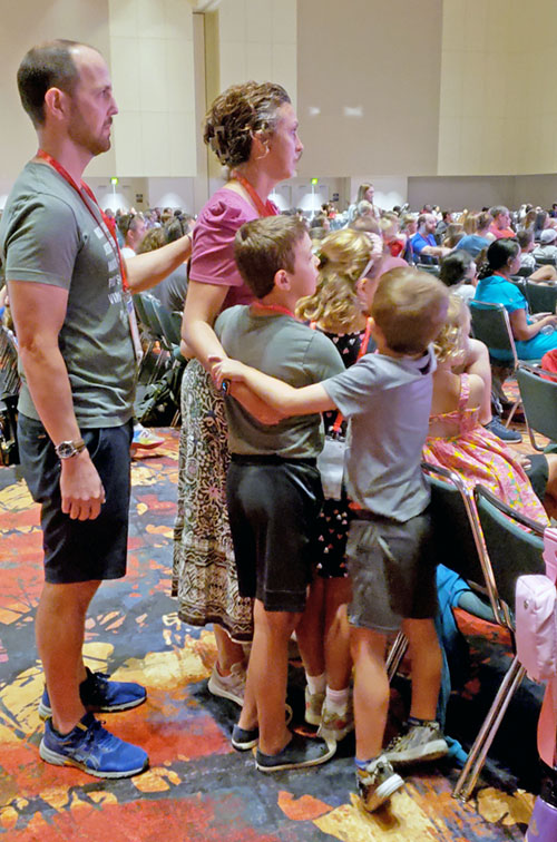 David Rafferty places a hand in prayer on the shoulder of his wife Katherine, as do their five children, during a time of prayer in the July 20 Cultivate (Family) Impact Session at the Indiana Convention Center in Indianapolis during the National Eucharistic Congress. The Rafferty family is from the Diocese of Des Moines, Iowa. (Photo by Natalie Hoefer)