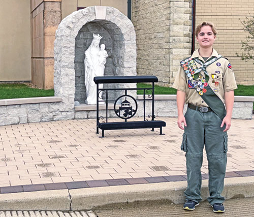 Andrew Hostetler, a member of St. Malachy Parish in Brownsburg, poses by a Marian grotto on the grounds of the Indianapolis West Deanery faith community. He oversaw the planning and fundraising for the project and took part in the manual labor of constructing it as part of an Eagle Scout project he completed. (Submitted photo)