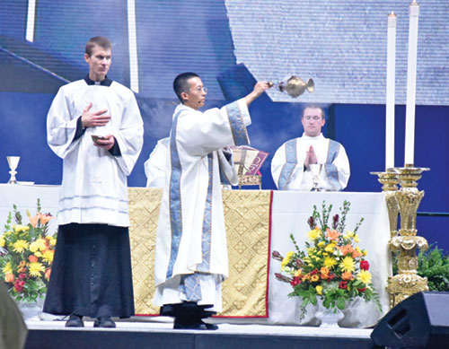 Transitional Deacon Khaing Thu incenses the 16,000 Catholic teenagers worshipping on Nov. 22 at the closing Mass of the National Catholic Youth Conference at Lucas Oil Stadium in Indianapolis. Seminarian Casey Deal, left, assists Deacon Thu. At right, transitional Deacon Samuel Hansen stands at the altar in the stadium. All are archdiocesan seminarians. (Photo by Sean Gallagher)